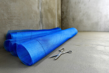 Blue fiberglass reinforcing mesh and scissors for applying construction layer on insulated wall or...