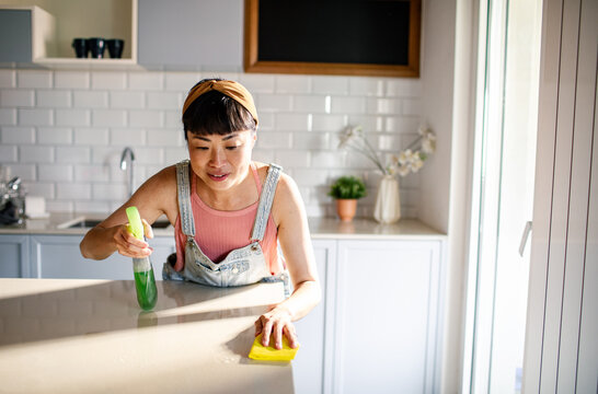 Asian woman cleaning kitchen counter with spray bottle and sponge