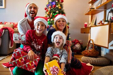 Family taking Christmas selfie with gifts and Santa hats