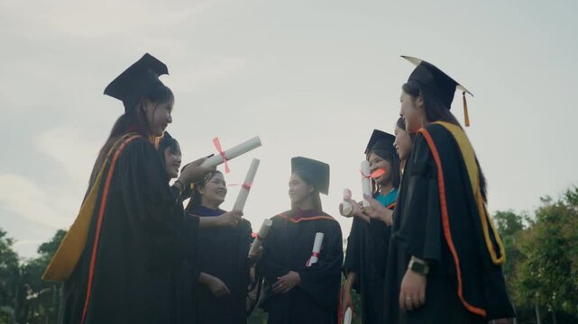 A group of women in graduation gowns are holding their diplomas. Scene is celebratory and proud