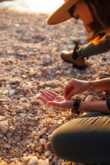 girl relaxing on the beach. a girl sits on the beach and collects various shells in her hand. hands with shells close-up.