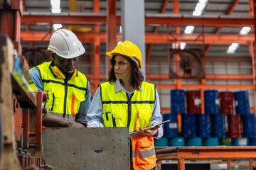 Female mechanical engineer is coaching and providing support to her trainee while examining the functions of metal machines in a factory. Teamwork between two engineers in a factory production plant
