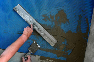 Applying construction glue layer on insulated floor for covering fiberglass reinforcing mesh.