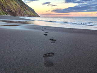 Footprints on a sandy volcanic beach at the sunset. Footsteps on the shore. Freedom, travel, path or loneliness concept