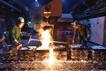 Group of workers in an iron foundry - casting a workpiece with liquid hot metal into a mold - cooperation and work safety