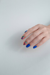 Nail art with blue gel varnish and floral design on woman's hand. Manicure salon service. White background, copy space. Vertical shot