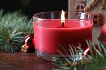 Burning candle, Christmas decor and fir tree branches on wooden table, closeup