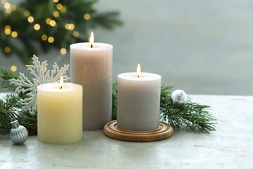 Burning candles, baubles and fir tree branches on white textured table, closeup
