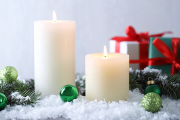 Burning candles, baubles and fir branches on artificial snow, closeup. Christmas atmosphere