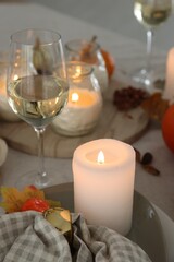 Burning candles, glass of wine and autumn decor on table, closeup