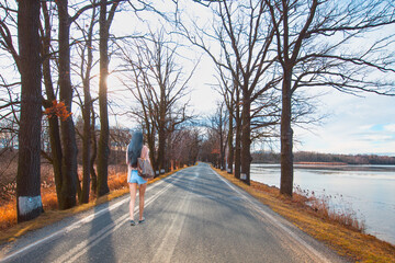 beautiful young woman in mini shorts walking alone on an asphalt road lined with trees in winter