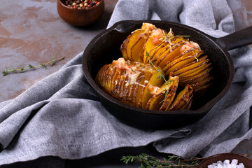 Hasselback potato roasted with cheese, bacon and aromatic herbs served in cast iron skillet. Hot meal