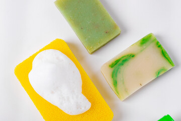 Flat lay with body sponge with foam and different bars of soap on white. Body care and hygiene products