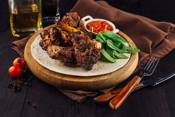 Grilled lamb ribs served on tortilla with spinach and sauce on wooden board