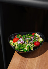 Fresh vegetable salad with tomatoes, cucumber and red onion in black bowl on wooden table