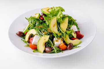Fresh salad with avocado, feta cheese and olives served on white plate