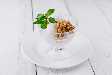 Vanilla ice cream served with walnuts and mint leaves on white rustic background