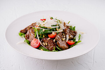 Salad with warm beef, tomatoes, arugula, parmesan and pine nuts on white plate