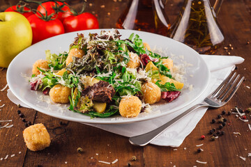 Salad with fried cheese balls, arugula, apple slices and spices being served on rustic wooden table