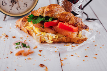 Delicious croissant filled with ham, scrambled eggs and tomato for breakfast