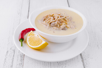 Turkish tripe soup is served on a white wooden table with lemon and pepper