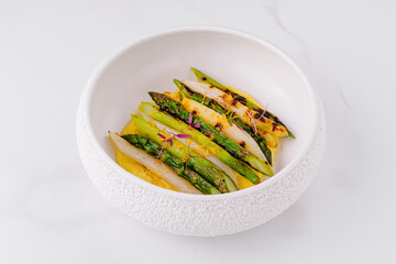Grilled white and green asparagus lying on yellow cream in white bowl