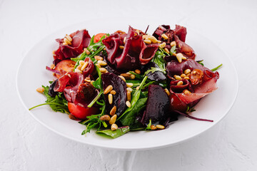 Salad with prosciutto, beetroot, arugula, pine nuts and sun-dried tomatoes on white plate