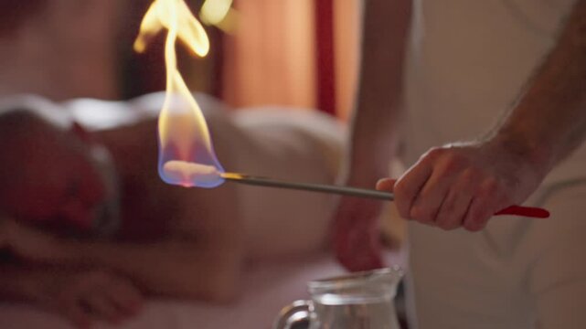 Close-up of Therapist Holding Fire Cupping Torch While His Male Client Lies in the Background Ready for Cupping Therapy. Concept of Alternative, Traditional, Chinese Medicine, Treatment