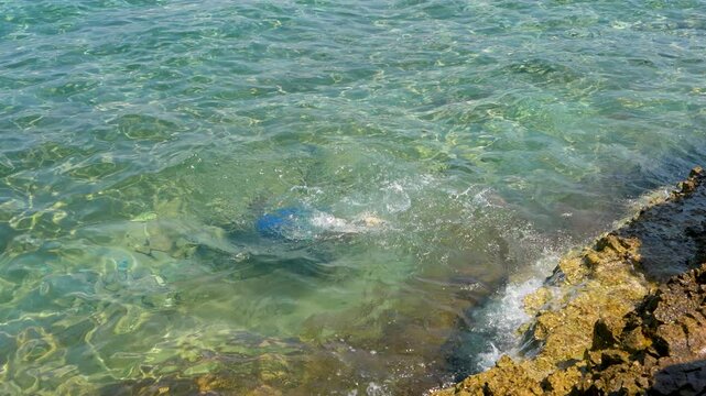  Boy in mask dives in crystal clear sea, playing in vde and observing  underwater world against bright sun.