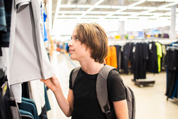 teenage boy chooses clothes for himself in a store