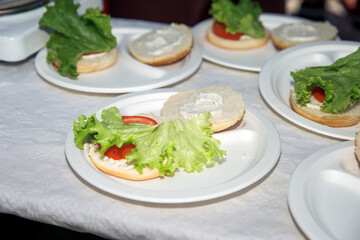Open face sandwich preparation with fresh lettuce, tomato, mayo, on paper plate, healthy eating concept