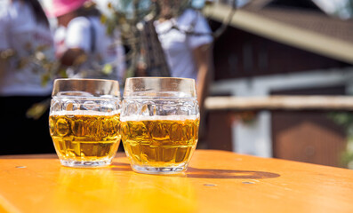 Two clear glass mugs filled with light beer on wooden table, outdoors, sunny day, casual gathering, refreshment, relaxation, beer mugs concept