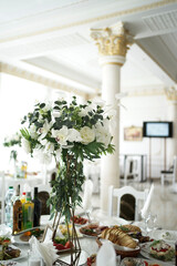 The festive table in the restaurant is decorated with a beautiful bouquet of white flowers.