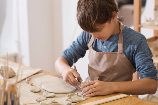 teenager boy works with clay makes  ceramic plate in pottery school.  Children arts a crafts class in workshop. child sculpts from clay