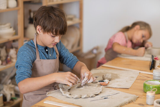 kids works with clay makes  ceramic plate in pottery school.  Children arts a crafts class in workshop. 