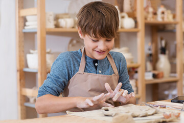 teenager boy works with clay makes  ceramic plate in pottery school.  Children arts a crafts class in workshop. child sculpts from clay © ulza