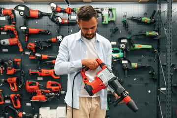 Plural perforator in hands. Man is in the hardware shop