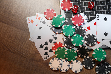 Poker chips, laptop, playing cards and dices on wooden table, flat lay. Online game