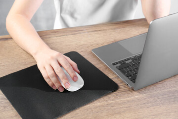 Woman using computer mouse while working with laptop at wooden table, closeup