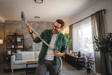 Adult man play air guitar with vacuum cleaner in modern living room