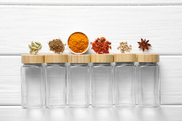 Different spices and glass jars on white wooden table, top view