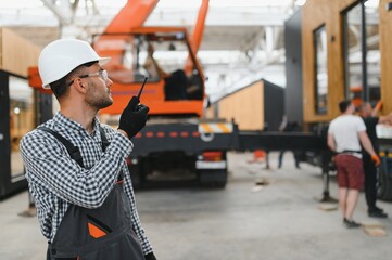 Foreman manages the loading of a prefabricated modular house to truck using walkie talkie