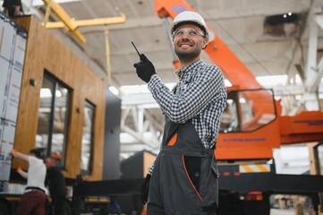 Foreman manages the loading of a prefabricated modular house to truck using walkie talkie