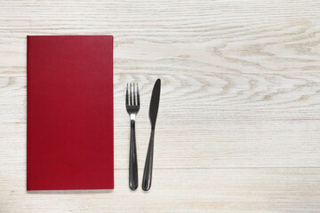 Hardcover menu and cutlery on white wooden table, flat lay. Space for text