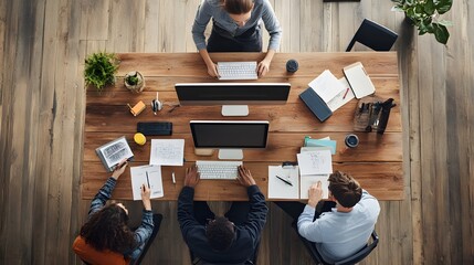 A Top View of a Collaborative Workspace with Four People Working at a Wooden Table