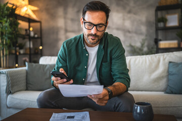 Adult man review bills and documents at home with cellphone and coffee