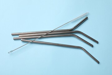 Metal drinking straws and cleaning brush on light blue background, top view