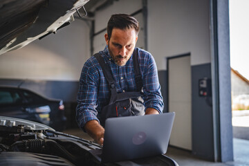 Car mechanic use laptop for car diagnostics in workshop garage bay