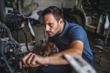 Car mechanic work on a car engine in a garage wearing blue shirt