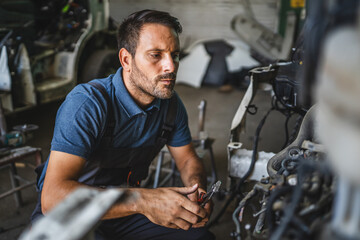 Car mechanic work on a car engine in a garage wearing blue shirt